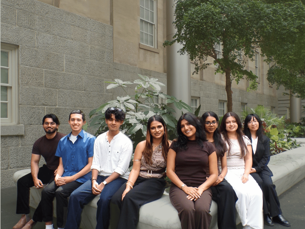 Students sitting in front of greenery smiling